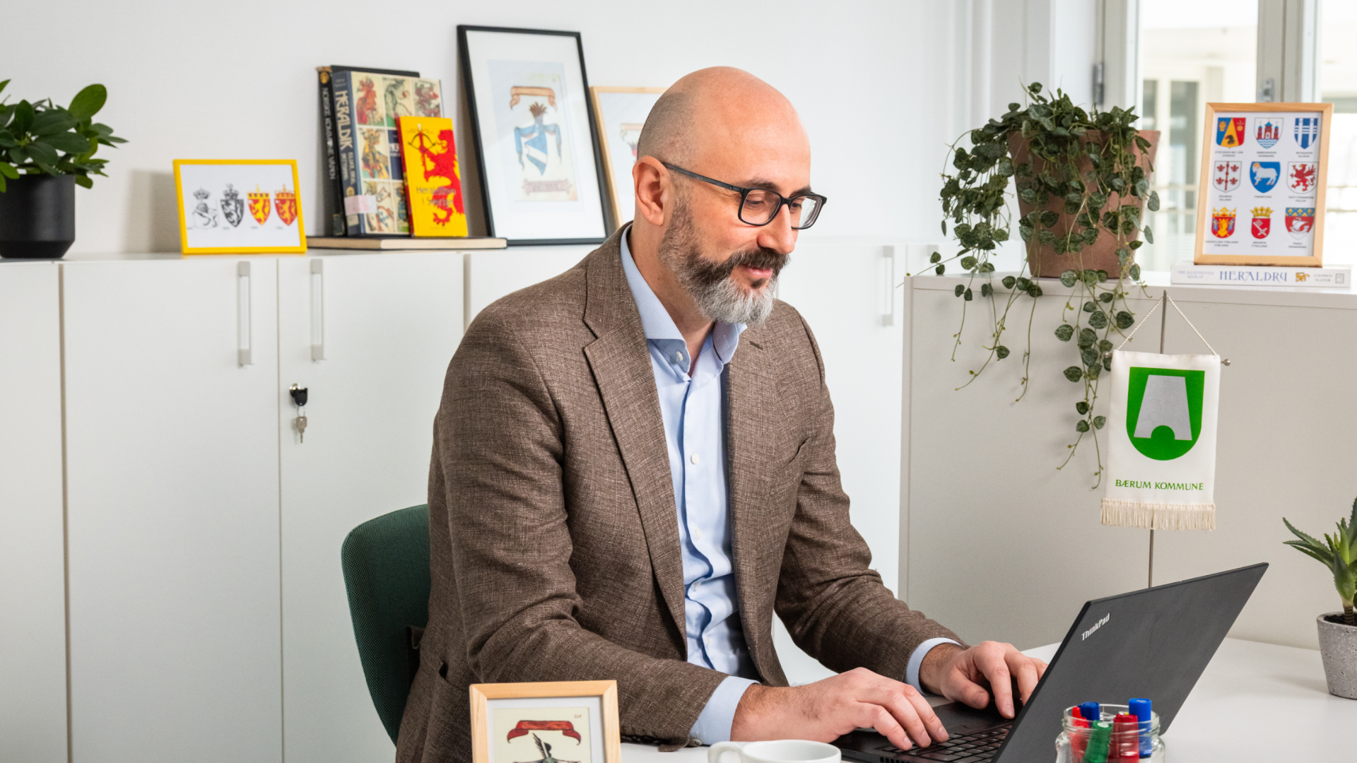 En mann med skjegg sitter i et kontorlandskap foran en PC.